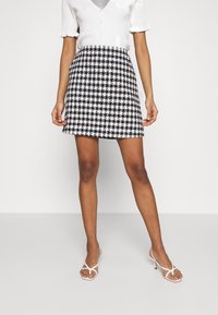 Mustavalkoinen houndstooth-minihelma, jossa on tekstuuriinen pinta, istuva vyötärö ja levenevä helma, yhdistetty valkoisiin korkokenkiin.