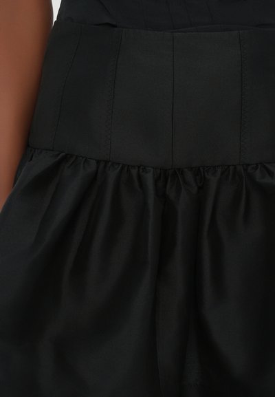 La tela del vestido negro presenta una textura suave, un corsé estructurado con costuras verticales y una falda amplia y con volumen.
