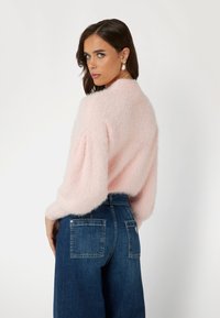 Flauschiger rosa Pullover mit hohem Kragen und Puffärmeln, kombiniert mit hochgeschnittenen dunkelblauen Jeans aus Denim mit Gesäßtaschen.