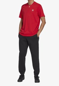 Röd bomulls t-shirt med rund halsringning och vit Adidas-logga, kombinerad med svarta avsmalnande joggingsbyxor och svarta sneakers.