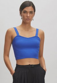 Blauwe geribbelde crop top met brede bandjes en een sweetheart halslijn, met een aansluitend ontwerp en een gladde textuur. Draagt met zwarte broeken.