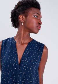 Haut sans manches bleu marine avec un décolleté en V, ornée de petits motifs floraux et d'un tissu doux et lisse. Subtiles accents argentés dans le design.