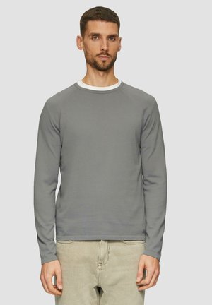 Grijze longsleeve shirt met een ronde hals, voorzien van een geribbelde structuur en een witte kraagaccent. Model draagt lichte spijkerbroek.