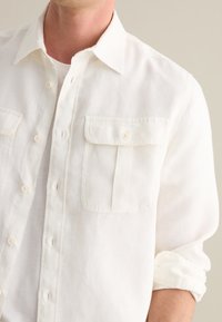 Camicia bianca di lino con colletto button-down, due tasche sul petto e maniche arrotolate, realizzata in un tessuto morbido e textured.