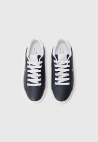 Juodų žemų sportbačių pora su baltais raišteliais ir padais, su Tommy Hilfiger ženklu ant liežuvėlio ir šono.