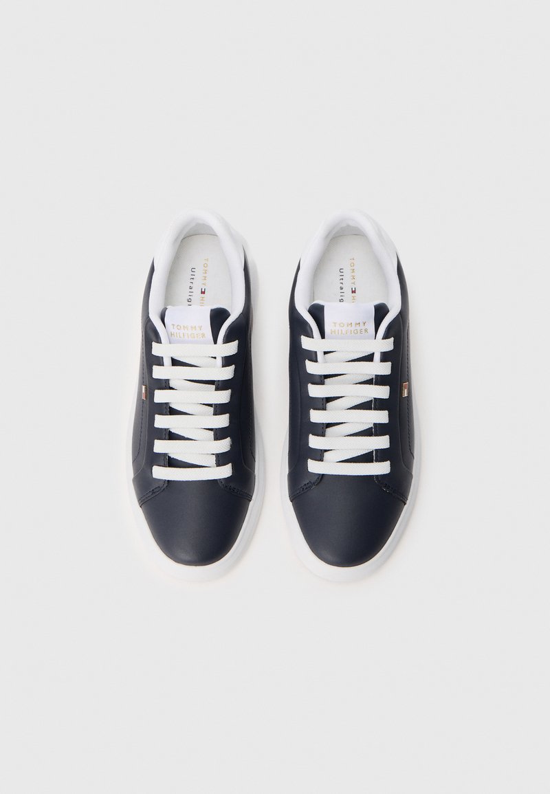 Par de zapatillas bajas negras con cordones y suelas blancas, que cuentan con la marca Tommy Hilfiger en la lengüeta y el costado.