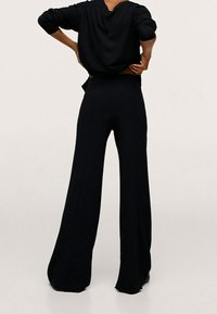Pantalons larges noirs à taille haute, en tissu doux, avec une texture lisse et un design épuré et minimaliste.