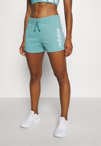 Turkoosiharmaat urheilushortsit, joissa on joustava vyötärö, sivutaskut ja valkoinen "adidas"-logo vasemmassa jalassa. Puuvillasekoitekangas.