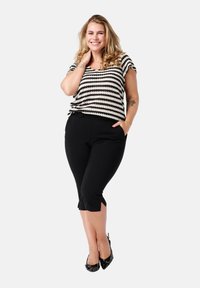 Zwarte cropped broek met zijsplitten, gecombineerd met een zwart-wit gestreept top. De outfit heeft een losse pasvorm en een zachte textuur.