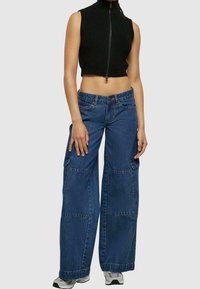 Svart ribbat crop top med hög krage, kombinerat med löst sittande blå denim cargo-byxor med sidfickor och en avslappnad silhuett.
