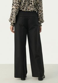 Black wide-leg pants with a smooth texture, featuring a high waist, back pockets, and a tailored fit. Worn with a leopard print blouse.