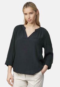 Zwarte blouse met lange mouwen, een V-hals en geplooide details rond de halslijn. Gemaakt van een soepele, lichte stof. Licht losvallende pasvorm.