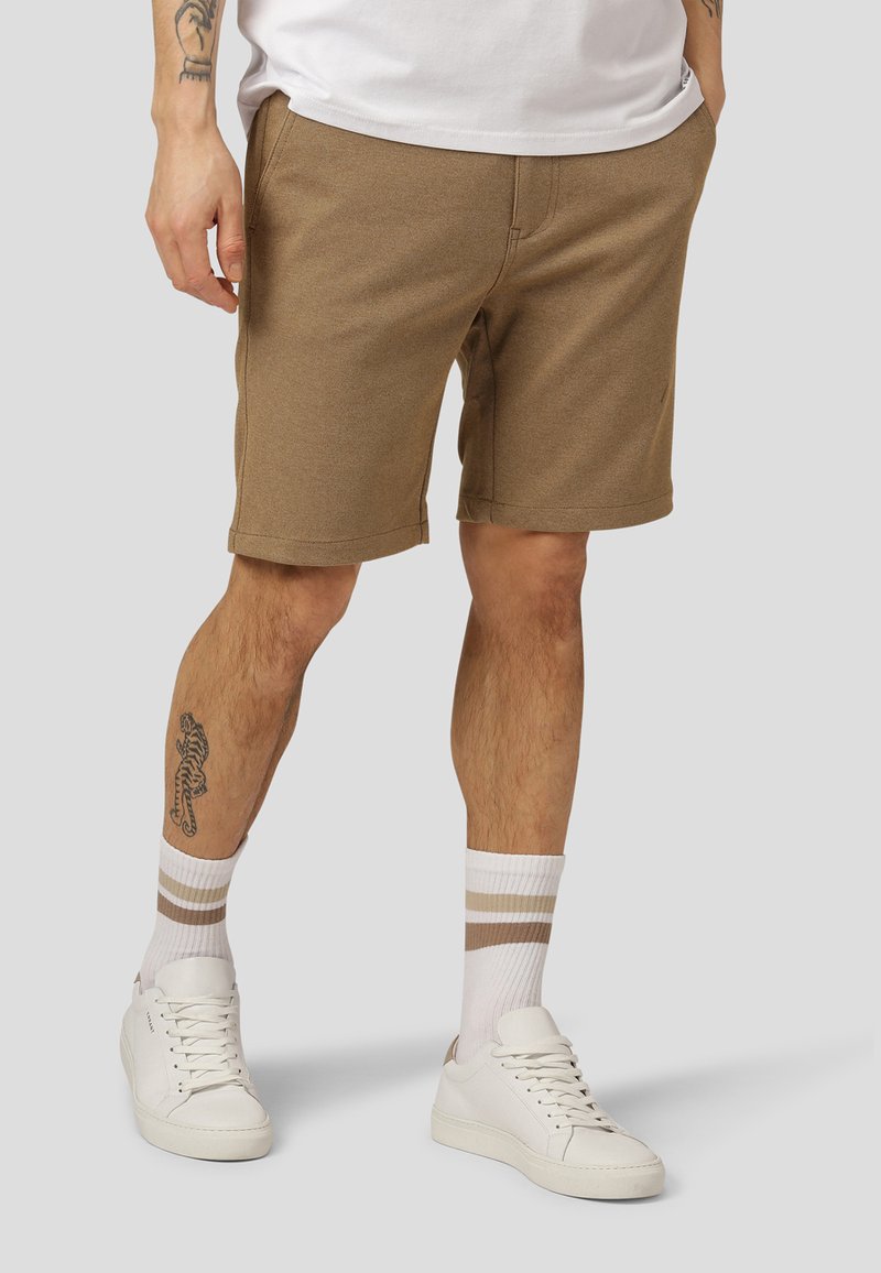 Brune bomullsshorts med en avslappet passform, med subtile tekstur- og sømdetaljer, kombinert med hvite joggesko og stripete sokker.