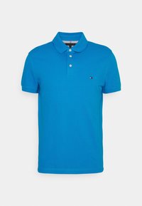 Modrá polo košile s krátkým rukávem se třemi bílými knoflíky a malou vyšitou nášivkou na levé hrudi.