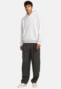Hellgrau, Kapuzen-Sweatshirt mit einer vorderen Tasche und geripptem Saum, kombiniert mit dunkelgrauen, lässigen Hosen. Leinenschuhe mit weißen und roten Akzenten.