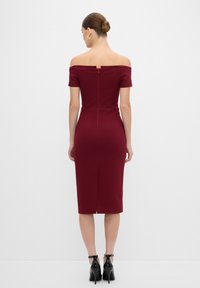 Burgundská off-shoulder šaty s krátkými rukávy, přiléhavý silueta, ke kolenům, se zipem na zadní straně a rozparkem na lemu. Černé lodičky na vysokém podpatku.