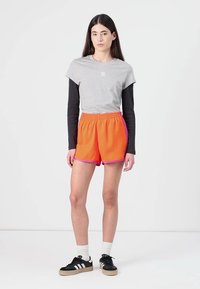 Shorts sportive portocalii cu marginile roz, asortați cu un tricou gri și mânecă lungă neagră. Pantofi negri cu accente albe și șosete.