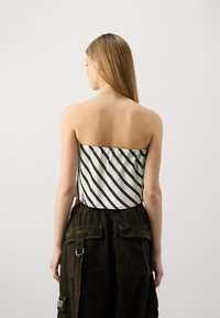 Haut sans bretelles blanc avec des rayures diagonales noires ; associé à un pantalon cargo vert foncé avec plusieurs poches et un détail métallique.