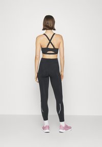 Svart sportbh med korsade axelremmar och utskärningsdetalj, tillsammans med svarta leggings med vita reflexdetaljer och rosa sneakers.