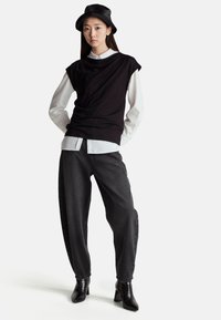 Černý top bez rukávů navrstvený přes bílou košili s límečkem, kombinovaný s volnými tmavými džíny a černými kotníkovými botami na podpatku. Součástí je kožený klobouk typu bucket.