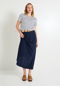 Falda maxi azul marino con un acabado texturizado, combinada con una camiseta de rayas en blanco y azul marino de manga corta y sandalias de plataforma de cuero marrón claro.