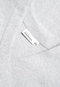 Lys grå sweatshirt lavet af blødt stof med V-hals design. Etiketten læser "Karen by Simonsen," størrelse M, med subtile teksturdetaljer.
