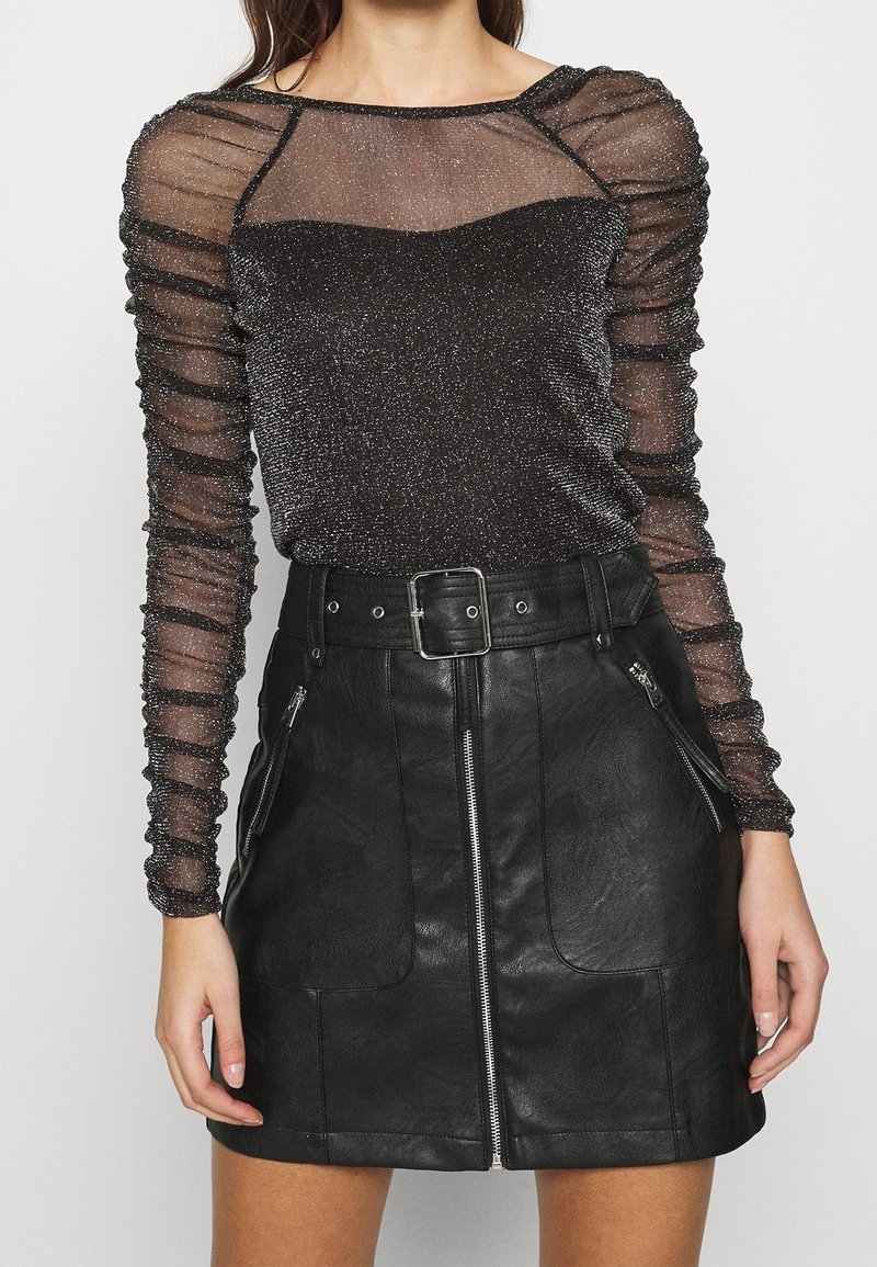 Svart texturerat konstläder minikjol med framdragkedjor, kombinerad med en genomskinlig, glittrig långärmad topp med rynkade ärmar.