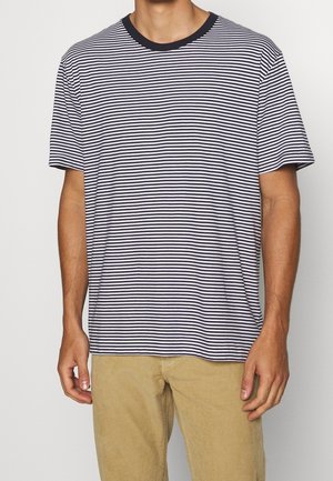 Stribet t-shirt i marineblåt og hvidt stof, korte ærmer, rund hals med en mørk kant, afslappet pasform, båret med lysebeige ribbukser.