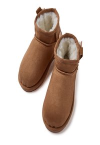 Botas de ankle marrones con un suave forro interior de felpa, textura lisa, punta redondeada y una asa trasera para facilitar el calzado.