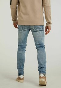 Beige långärmad skjorta, ljusblå slim fit jeans med viss blekning, och beige sneakers med vita accenter och texturerade sulor.