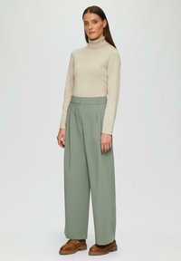 Beżowy sweter z golfem, dopasowany, w połączeniu z jasnoszarymi, szerokimi spodniami z wysokim stanem. Brązowe buty na platformie dopełniają stylizację.