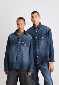 Denimskjorter i varierende nyanser av blått, med to brystlommer, knapplukking og en avslappet passform. Glatt tekstur og uformell design.