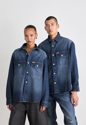 Camicie in denim in diverse tonalità di blu, con due tasche sul petto, chiusura con bottoni e vestibilità rilassata. Texture morbida e design casual.