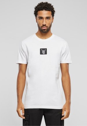 Hvid bomulds t-shirt med et sort rektangulært patch med et grafisk design af håndsymboler på brystet. Korte ærmer og rund hals.