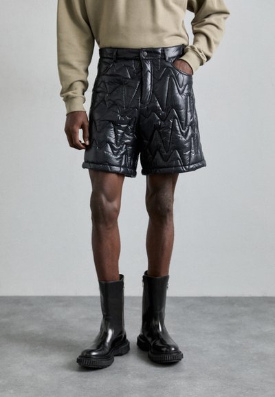Shorts noirs matelassés avec des motifs en zigzag, dotés d'une fermeture à bouton à l'avant et de poches latérales, associés à des bottes noires brillantes jusqu'aux genoux.