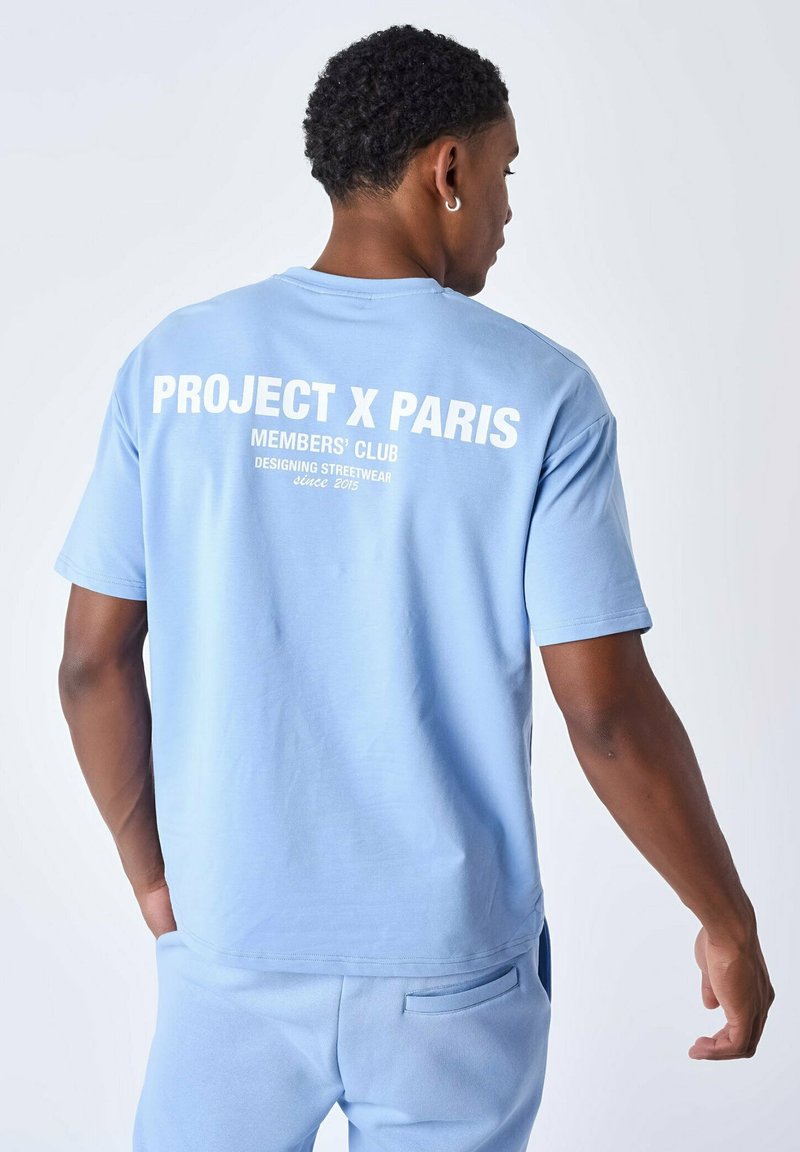 Lichtblauwe katoenen t-shirt met een ronde hals en korte mouwen. Het ontwerp op de achterkant bevat witte tekst: "PROJECT X PARIS MEMBERS' CLUB sinds 2015."
