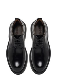 Chaussures de ville en cuir noir avec une finition brillante, bout rond, design à lacets et semelle en caoutchouc robuste. L'intérieur présente un rembourrage marron.