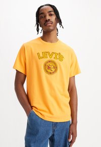 Sárga pamut póló rövid ujjakkal és kerek nyakkivágással. Elülső részén piros és sárga "LEVI'S" grafikai nyomattal.