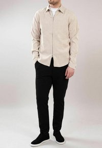 Beige teksturert zip-up skjorte med lange ermer, kombinert med svarte slim-fit bukser og svarte sneakers med hvite såler.