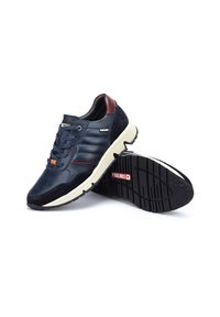 Baskets en cuir et daim bleu marine avec une semelle en caoutchouc blanche, présentant des détails rayés et un accent bordeaux au niveau du talon. Logo sur le côté.