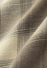 Detailní záběr na béžovou a hnědou kostkovanou látku ukazující tkanou strukturu a protínající se čáry s jemnými záhyby.