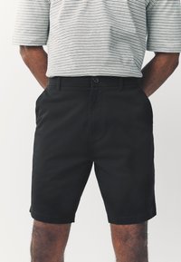 Zwarte katoenen korte broek met een rechte snit, zijzakken en een knoopsluiting. De stof oogt glad met een subtiele glans.