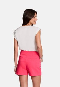 Witte mouwloze top met een gebogen rand, gecombineerd met felroze shorts met achterzakken en een aansluitende taille. Glad stoftextuur.