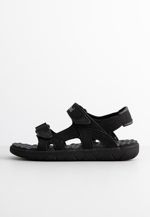 Sandales noires au design sportif, dotées de brides en synthétique, de fermetures Velcro ajustables et d'une semelle en caoutchouc texturée.