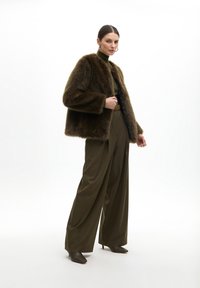 Brown fur cropped coat with long sleeves, olive green fitted sweater, high-waisted wide-leg trousers, and pointed brown heeled boots.