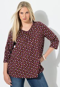 Top burdeos con escote en V, mangas de ¾ y un estampado floral que presenta flores en tonos rosas, blancas y marrones. Tejido suave, corte relajado.