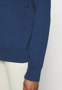 Sudadera azul marino con un bolsillo tipo canguro, puños y dobladillo de canalé, hecha de un suave material de algodón con una textura lisa.