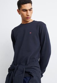 Felpa blu navy in cotone con colletto girocollo e polsini elasticizzati; presenta un piccolo design ricamato in rosso e bianco sul petto.