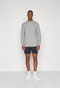 Grauer Sweatshirt, Rundhals, gerippte Bündchen. Kombiniert mit dunklen Shorts und weißen Sneakers. Einfaches Design, keine sichtbaren Muster oder Logos.