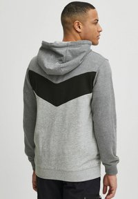 Gray hoodie with a black chevron pattern on the back. Features a drawstring hood and ribbed cuffs, made from a soft fabric.